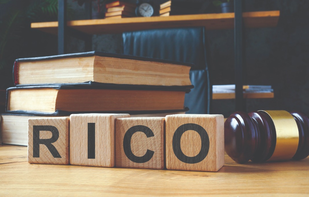 Stack of books and gavel behind wooden blocks that spell RICO